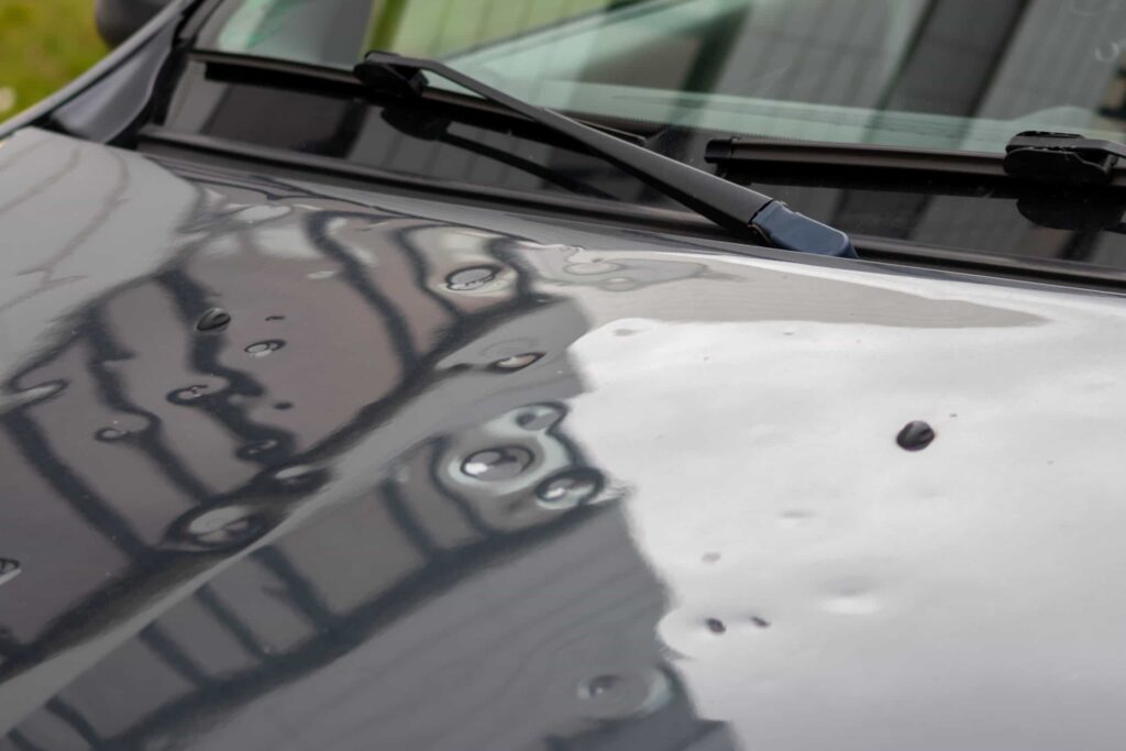 Close-up of hail damage on car hood awaiting repair 